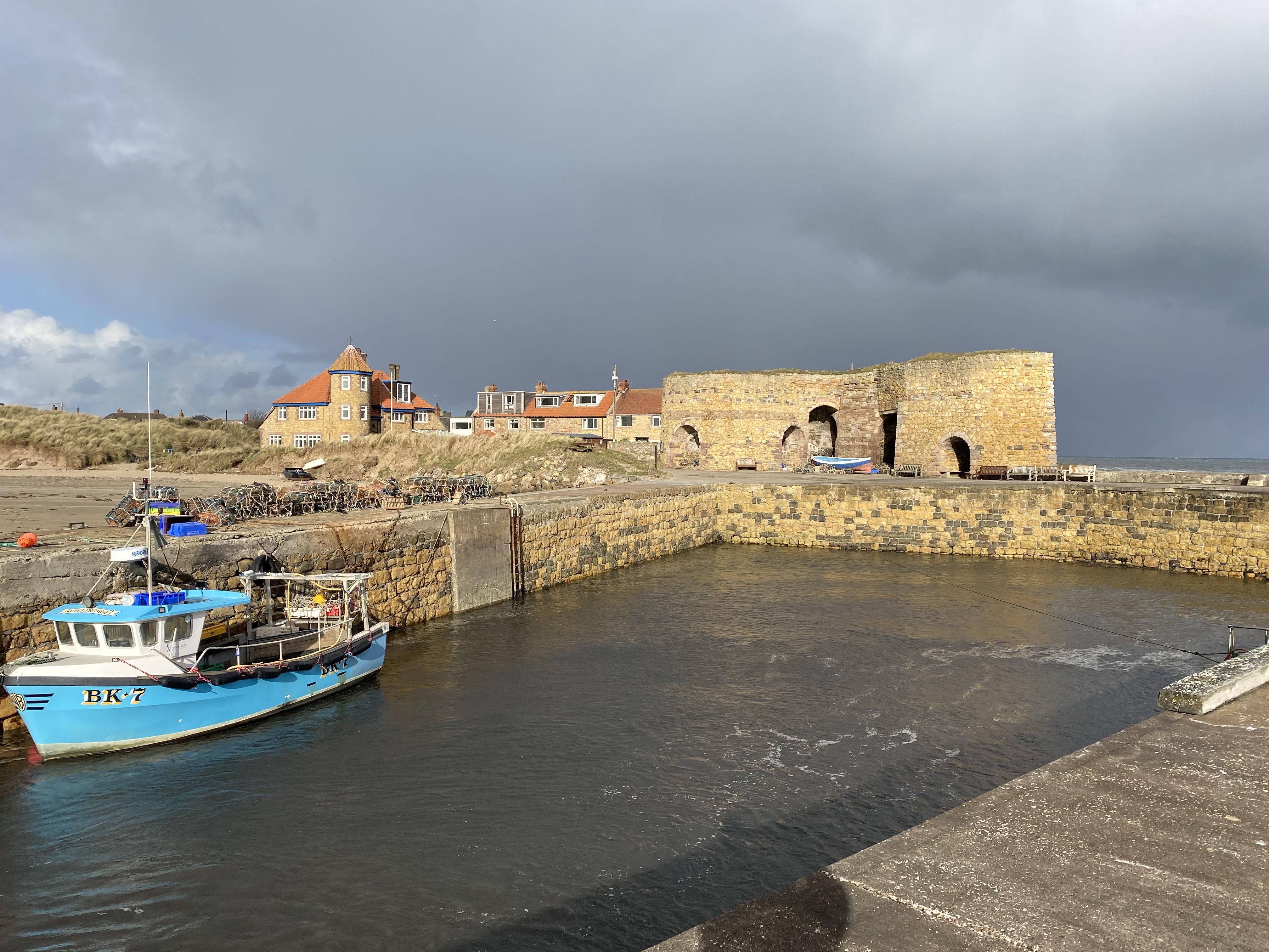 A sky heavy with rain illuminating Beadnell lime kilns. A single arctic blue boat is moored up.