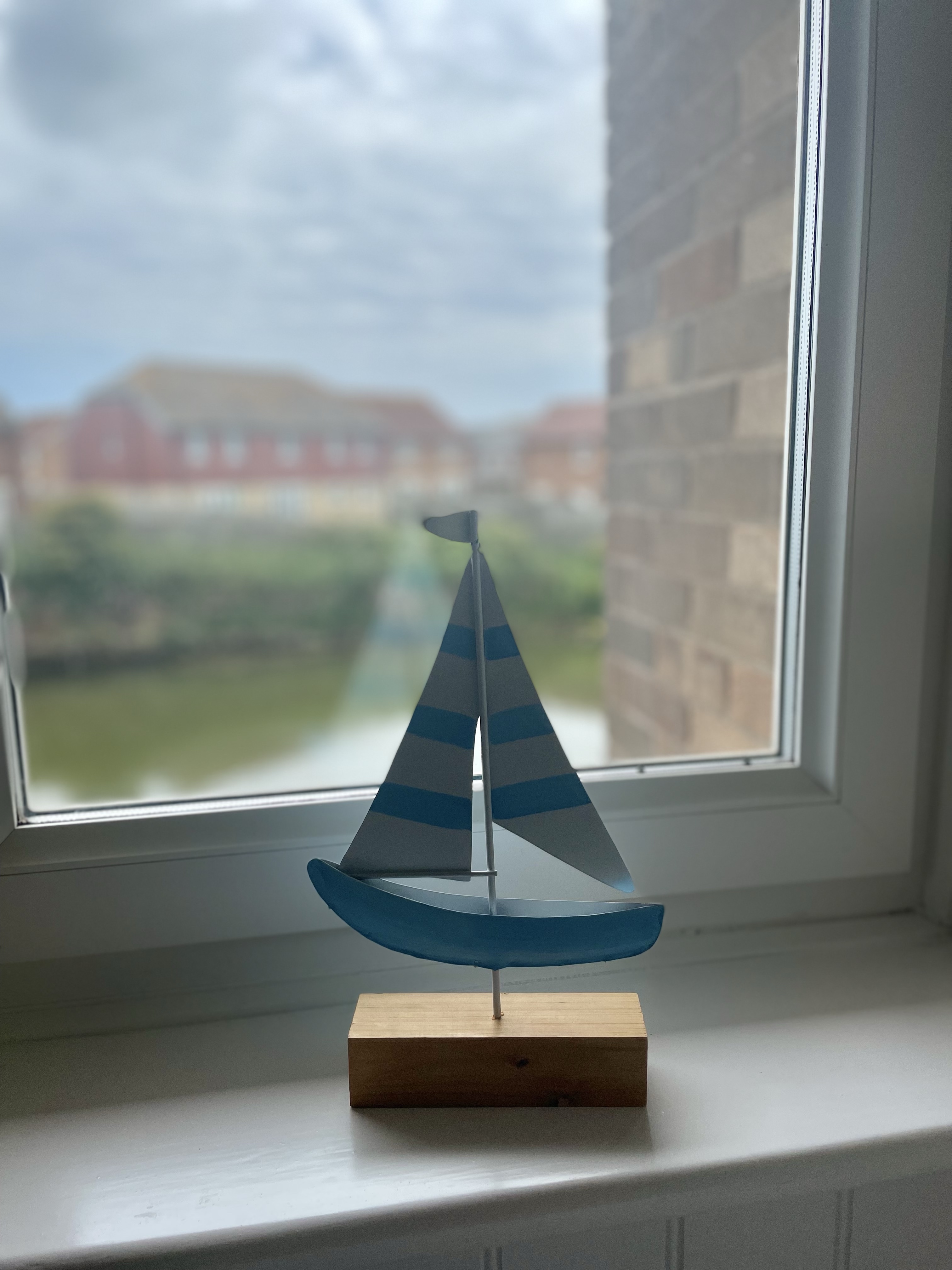 A small wooden boat, with stripy sails, is sat on a windowsill